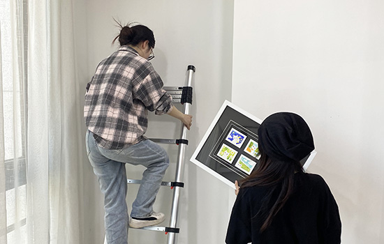 Две девушки используют en131 телескопическую лестницу, чтобы повесить картину.