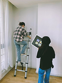 две девушки используют лестница алюминиевая телескопическая en131 для подвешивания картин
